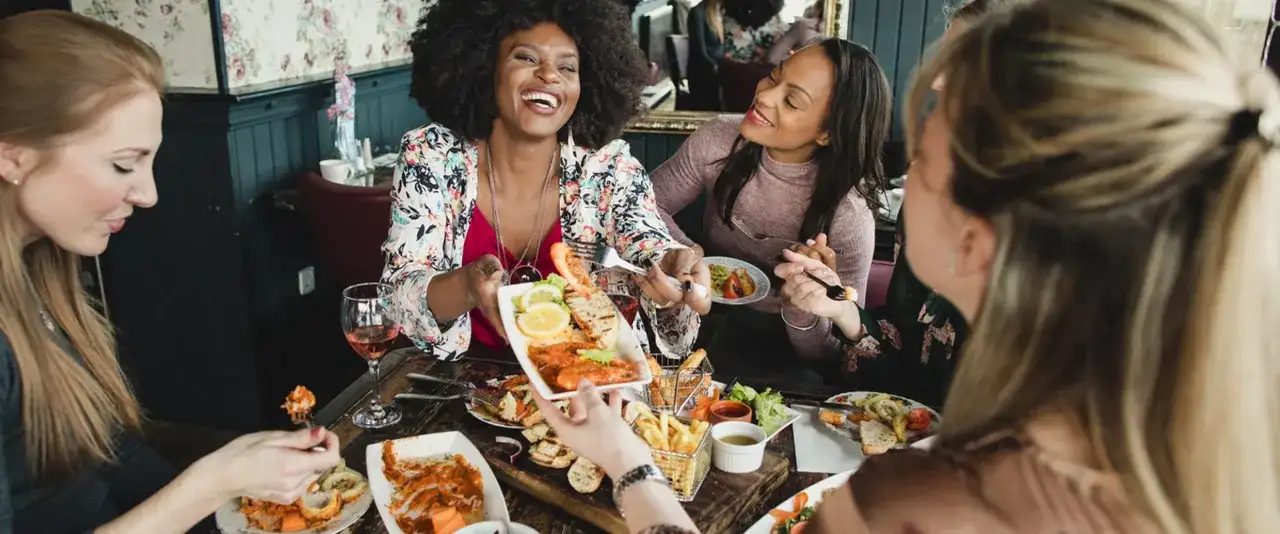 Vier Freundinnen genießen einen köstlichen Brunch in Berlin. Sie lachen und teilen sich Speisen wie Garnelen und Pommes.