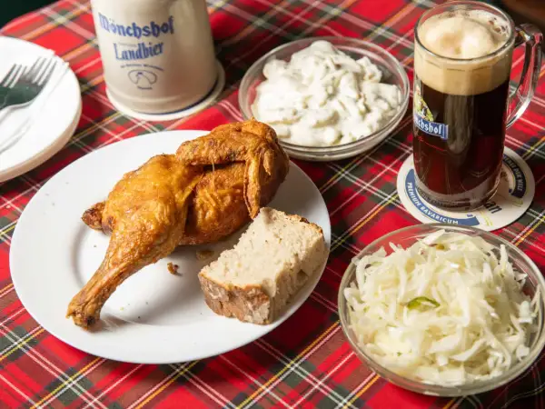 Knusprige Henne Berlin mit Brot, Krautsalat und einem Bierkrug.
