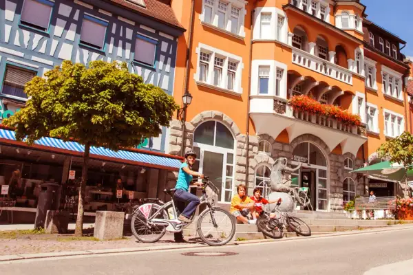 Familie genießt sonnigen Tag in der Stockach Altstadt. Kinder sitzen auf Treppen, Mutter auf Fahrrad.