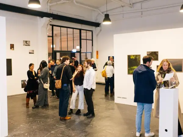 Besucher auf einer **Foto Messe Hamburg** diskutieren Kunstwerke in einer hellen Galerie.